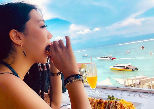 レンボンガン島の綺麗な海を見ながらランチを食べる女性モデル