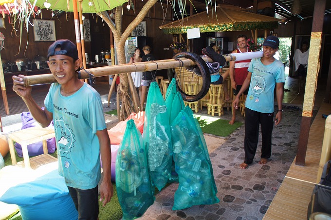 竹に吊るされた袋に入った沢山のゴミを担ぐボランティアの少年2人