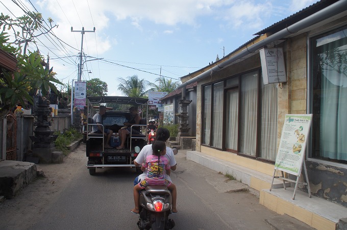 レンボンガン島のメイン通りを走る観光の車と2人乗りのバイク