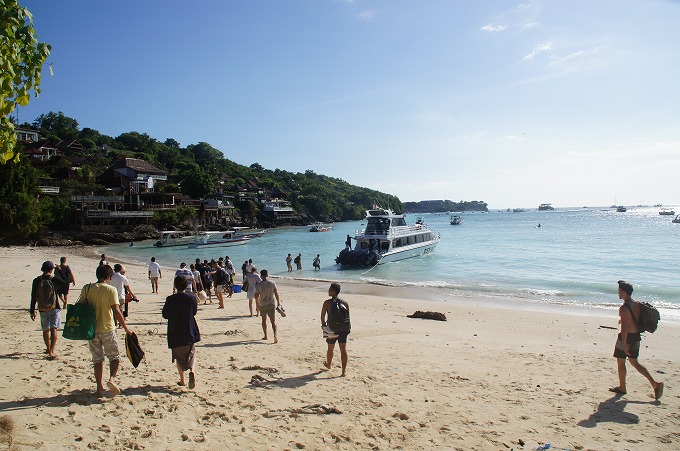 レンボンガン島のビーチを歩いて乗船を開始する観光客
