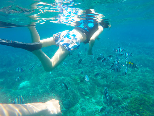 レンボンガン島のクリアーな海中で綺麗なサンゴやカラフルな熱帯魚と一緒に遊泳を楽しむ女性