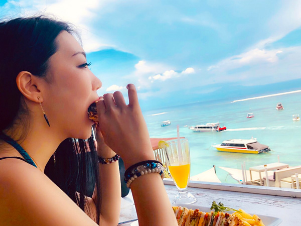 ルーフトップバーで食事をする女性とレンボンガンの快晴の空と海