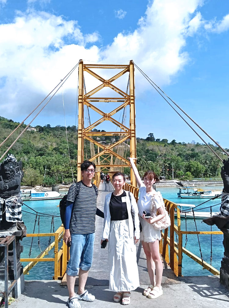 青い空とエメラルドグリーンの海に浮かび上がるイエローブリッジで記念撮影をするご夫婦と手をかかげる娘様の3人ご顔族様