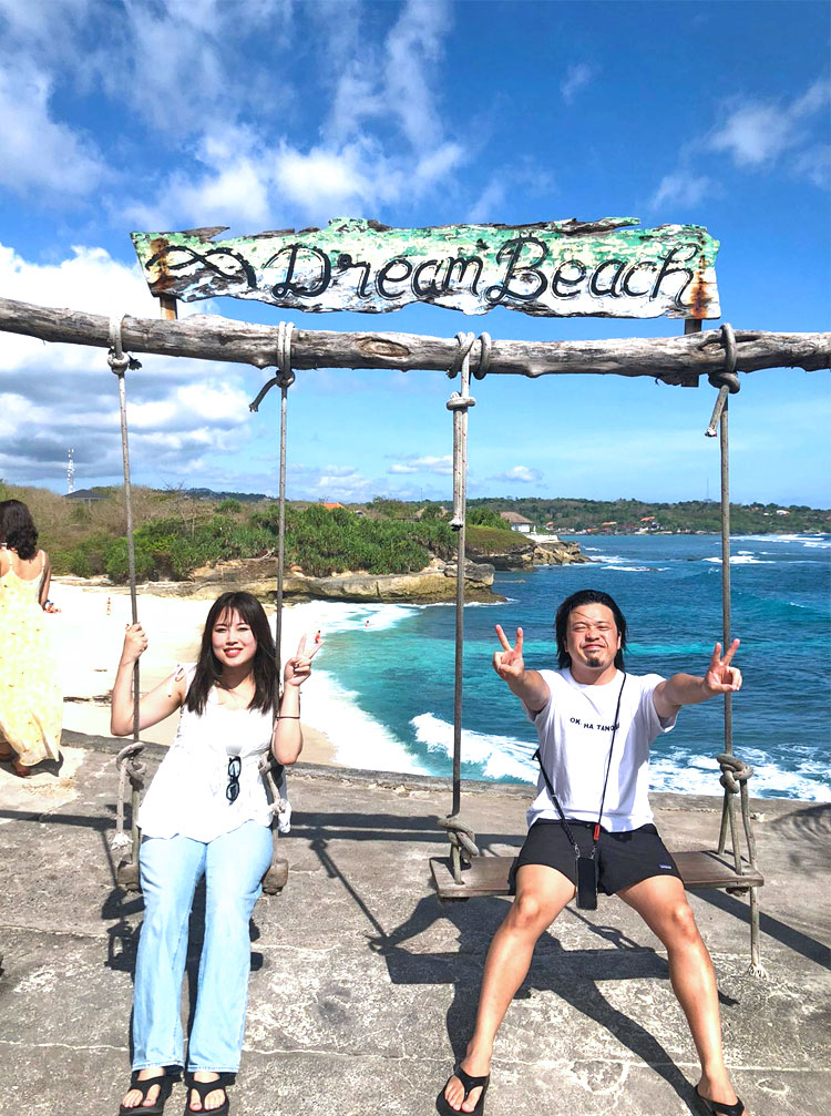 青い空とエメラルドグリーンの海とホワイトサンドが映えるドリームビーチのブランコにのるカップル