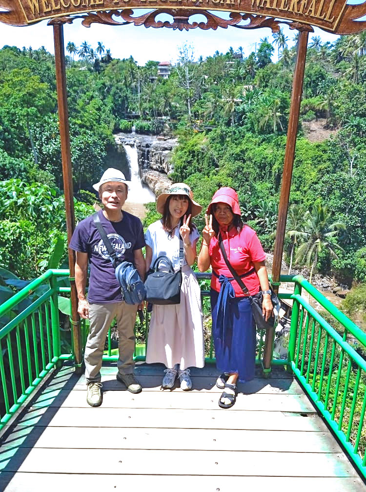 トゥグヌンガンの滝をバックにバリ姫の女性ガイドと一緒に笑顔のご夫婦