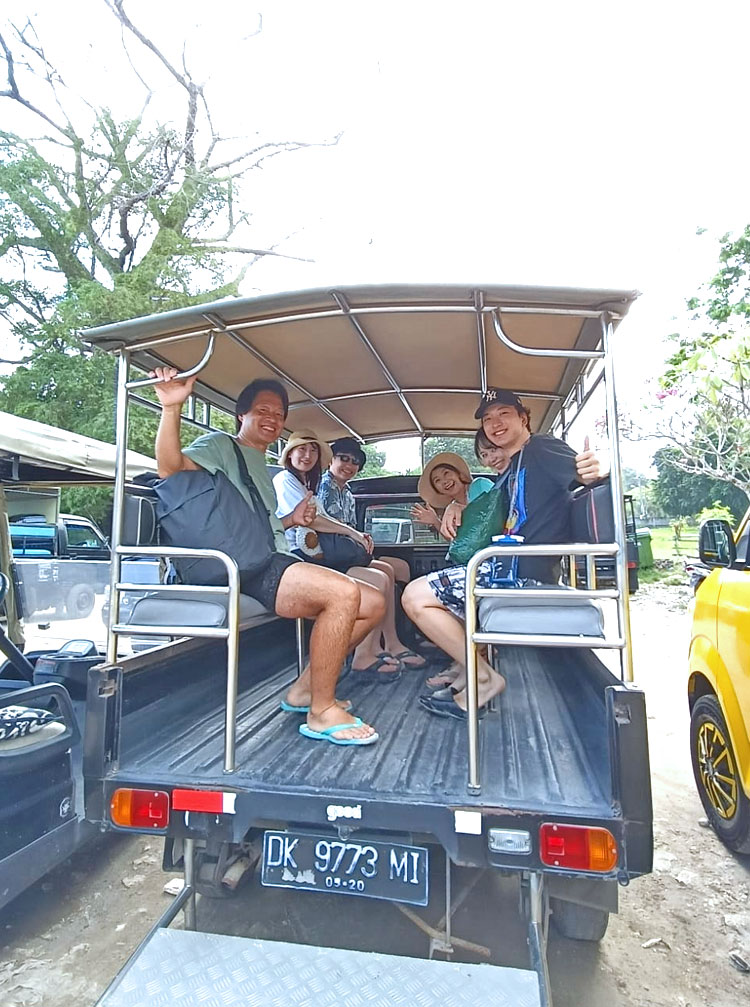 レンボンガン島での移動で使うオープントラックに乗車し、ガイドに手をふる笑顔の4人家族様