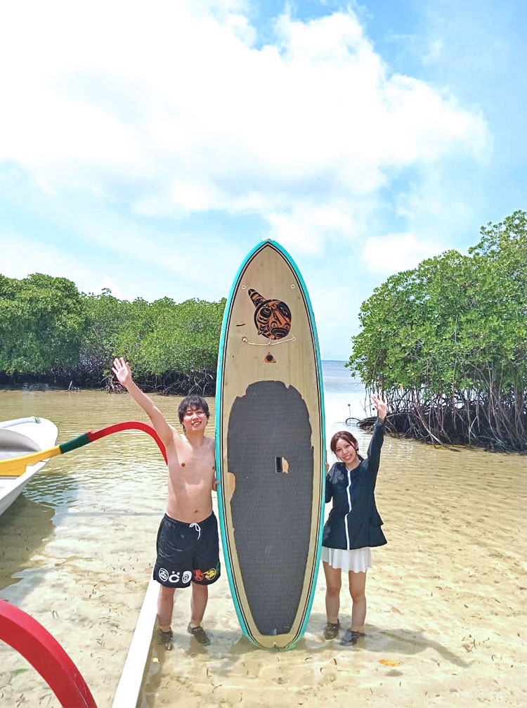 大きなSUPボードとオールをもって手をふる笑顔のカップル