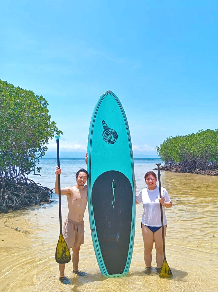 キレイな海とSUPと一緒に記念撮影をする笑顔のご夫婦