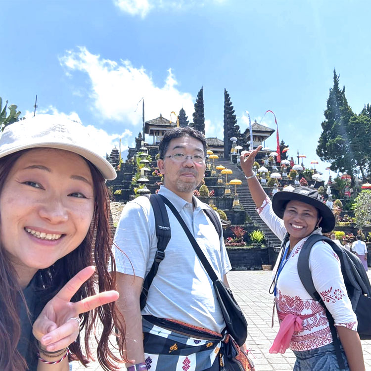 明るいバリ姫の女性ガイドと笑顔でブサキ寺院で記念撮影をするご夫婦様