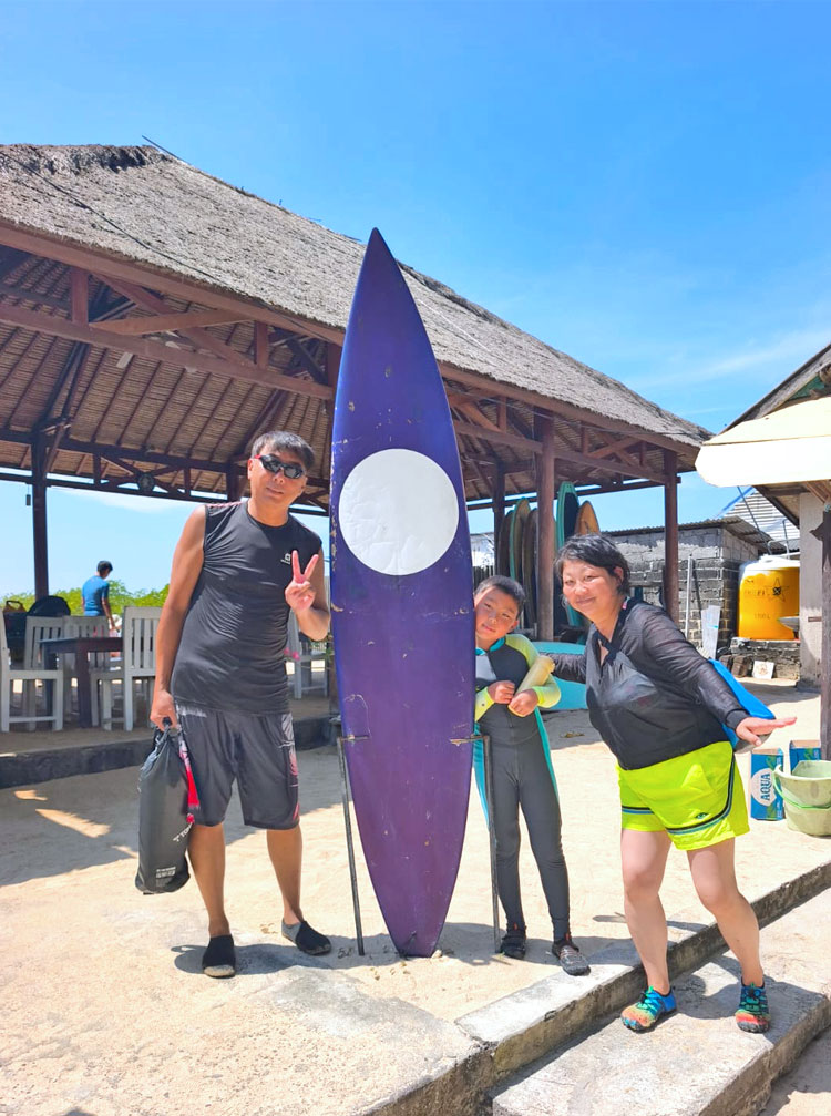 レンボンガン島でシュノーケリングに出発する前に大きなサーフボードと一緒に笑顔の3人家族様