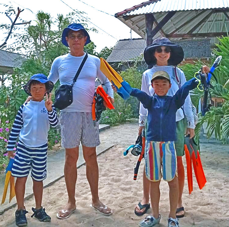 マンタシュノーケリングの準備をし、フィンをもつパパさんママさんと2人のお子様