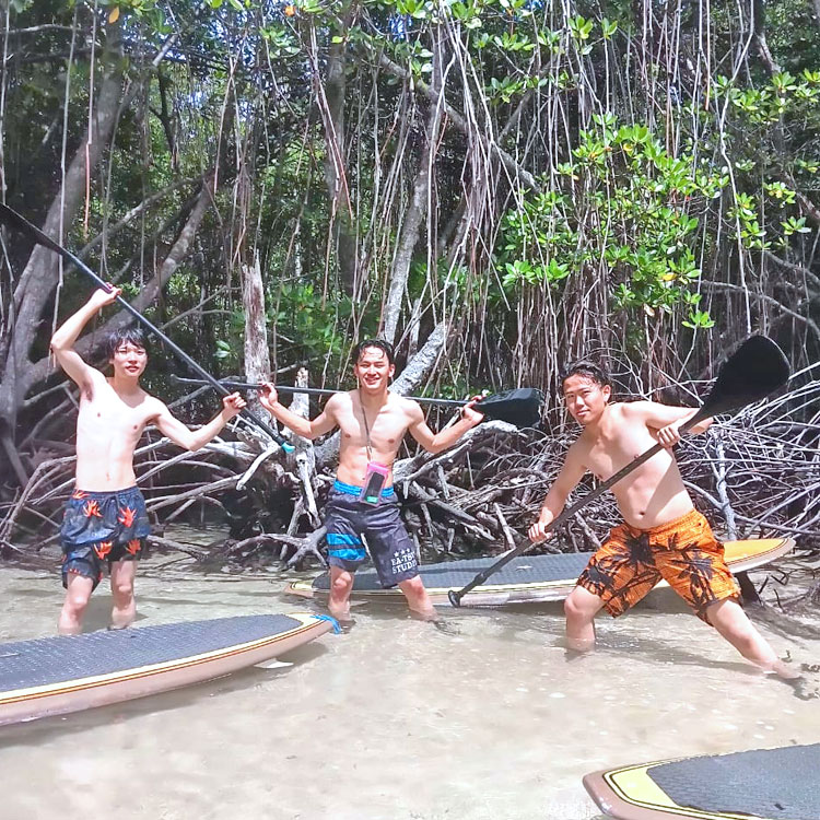 SUPの道具を持って各々ポージングをする仲良し男性3人組