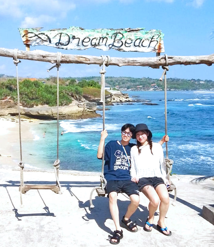 青い空とエメラルドグリーンの海とホワイトサンドが映えるドリームビーチのブランコにのるカップル