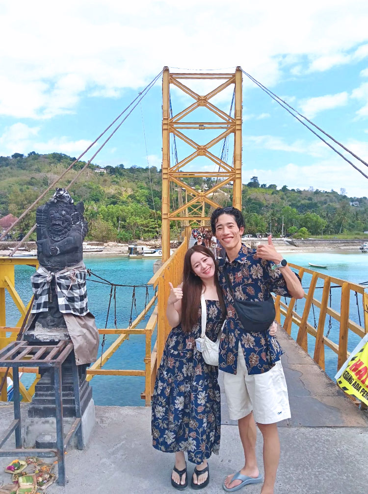 青い空とエメラルドグリーンの海に浮かび上がるイエローブリッジで記念撮影をするカップル