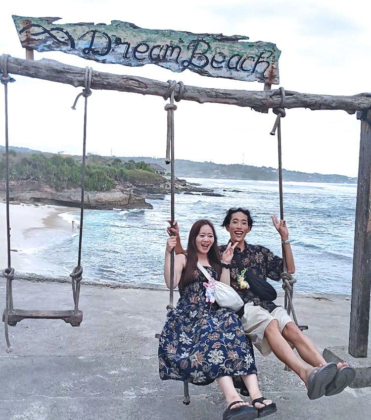 青い空とエメラルドグリーンの海とホワイトサンドが映えるドリームビーチのブランコにのるカップル