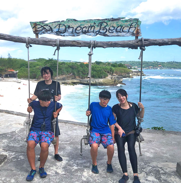 青い空とエメラルドグリーンの海とホワイトサンドが映えるドリームビーチのブランコにのる笑顔のご家族様