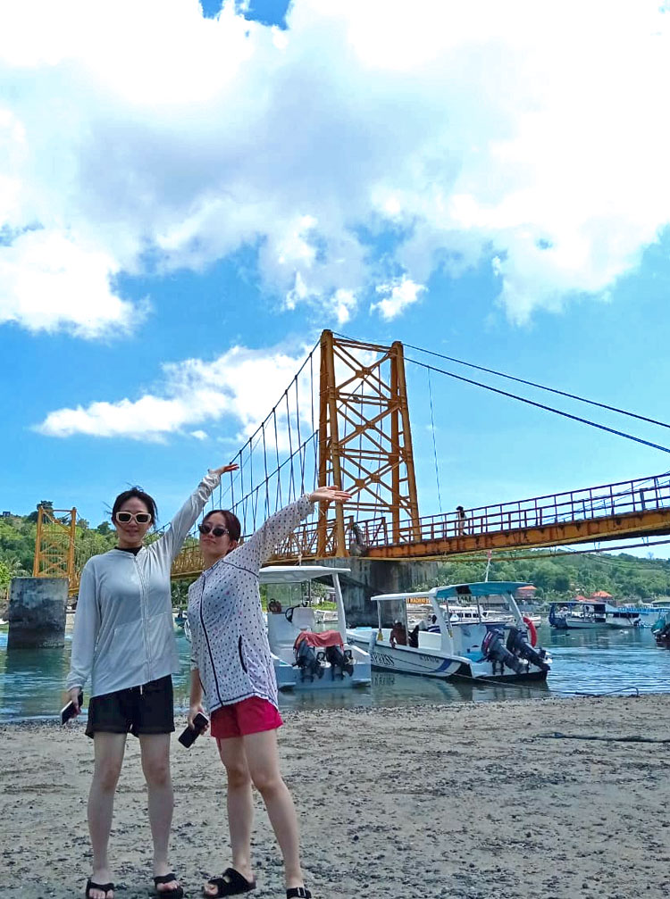 イエローブリッジが見える砂浜見て手を掲げる仲良しの女性2人組